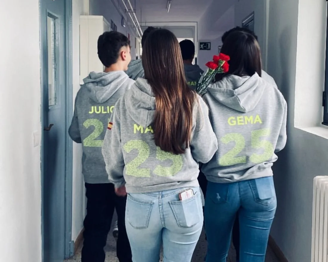 Grupo de espaldas con sudaderas grises personalizadas con nombres y el número 25 en amarillo.